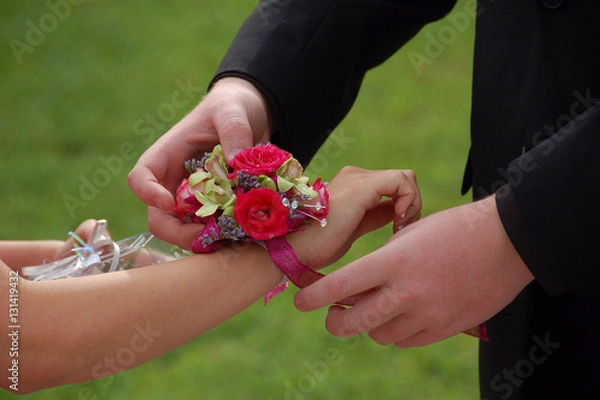 Obraz Young man slides wrist corsage onto prom date