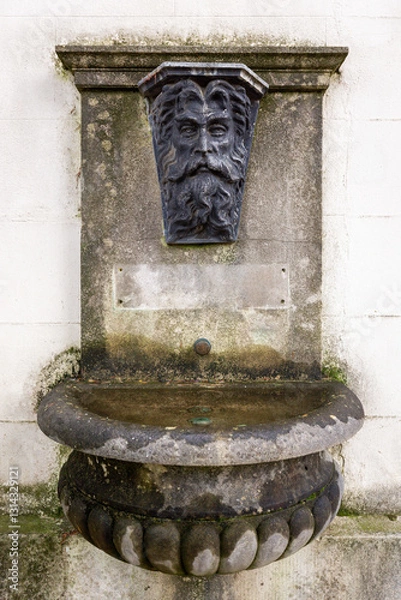 Fototapeta Stone Fountain with Grotesque Face Carving on Building Wall
