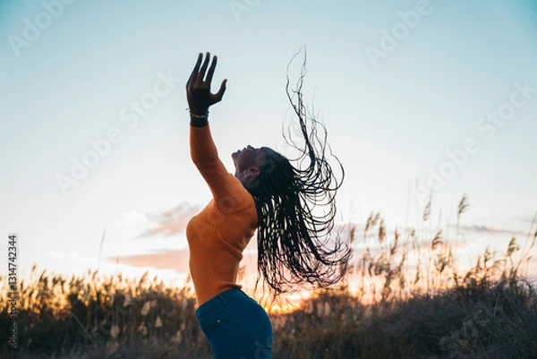 Obraz Young woman dancing with flowing hair at sunset in a field