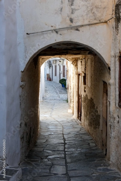 Fototapeta Narrow alley with tunnel and with whitewashed walls and stone pavement leading to a courtyard in the Greek Islands, Greece