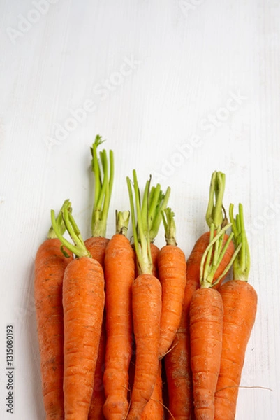 Fototapeta Aerial view of carrots with stem on white wooden table, vertical with copy space
