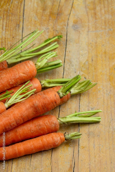 Fototapeta Top view of carrots with stem on wooden table, vertical with copy space