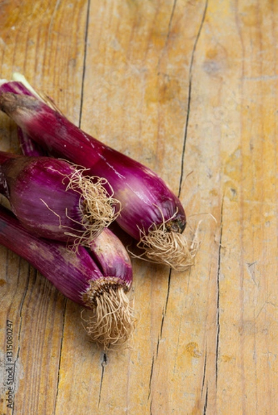 Fototapeta Top view of purple spring onions on wooden table, vertical with copy space