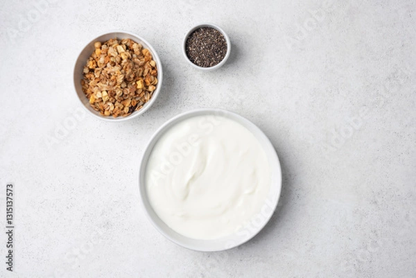 Fototapeta Bowl of greek yogurt, granola and chia seeds on a grey background. Top view with copy space for design elements or text. Plain white yogurt in bowl