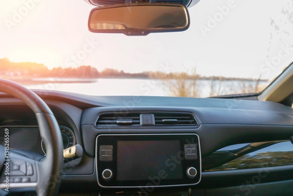 Fototapeta Car interior with a modern dashboard and rear-view window with serene lake with trees lining the shore, under a clear sky ckground