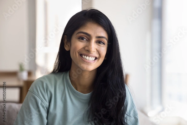 Obraz Head shot portrait of beautiful Indian female having attractive appearance, positive mood, posing for camera seated on sofa in living room with joyful expression, spend carefree leisure alone at home