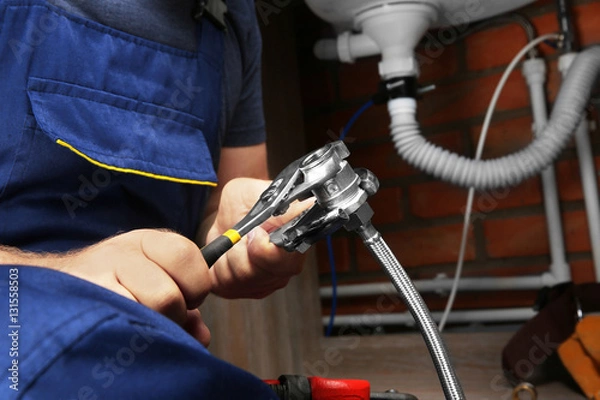 Fototapeta Hands of plumber connecting pipe union to flexible hose, close up view