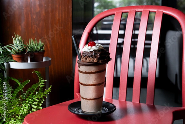 Obraz Indulgent mocha frappe topped with chocolate and a cherry, served in a stylish glass on a red chair in a cafeteria setting