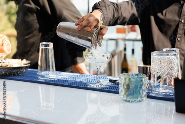 Obraz Male bartender pours a cocktail in a summer bar. Close-up of a bartender's hand pouring a drink from a silver shaker into a glass. A bartender makes a cool summer cocktail at the hotel bar outside