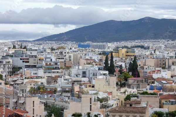 Fototapeta Athens cityscape expanding towards mountains under cloudy sky