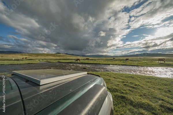 Fototapeta An electric SUV with a solar battery on the hood stands against the background of a green meadow and a river. Solar panel on the background of nature. Alternative green energy.