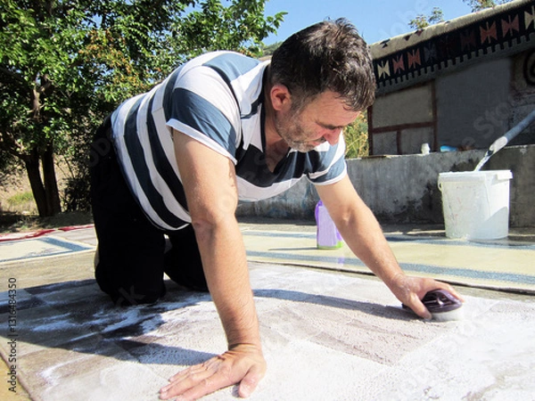 Fototapeta A man in the village washes the carpet with a brush