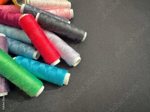 Obraz Colorful sewing thread spools on a dark fabric background with copy text space