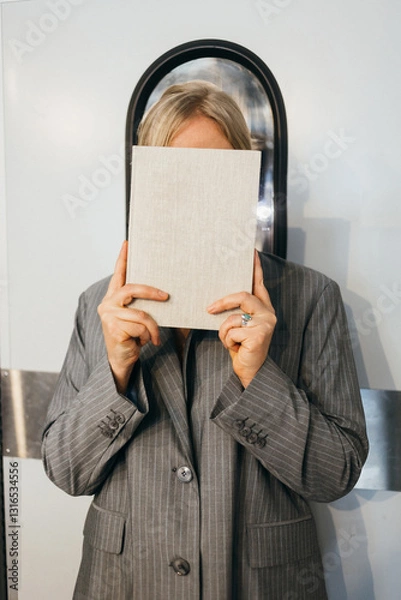 Fototapeta A stylish figure subtly conceals their true identity behind a plain book, sparking intrigue and curiosity