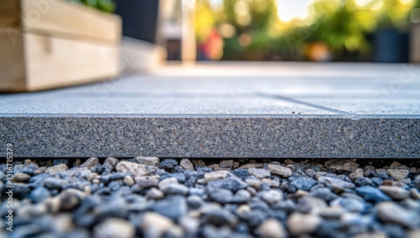 Fototapeta Close-up of the lower part of a garden paver showcasing its surface texture against small gravel, with greenery in the background