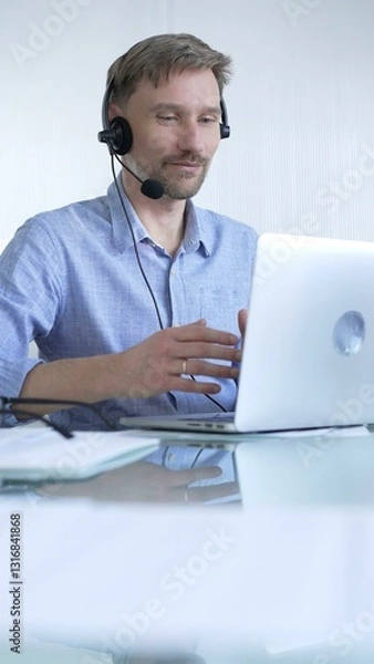 Fototapeta Male office worker demonstrates the significance of technology in modern business through client communication using laptop and headset. Business people concept