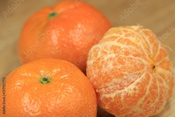 Fototapeta A group of ripe tangerines, some peeled, on a wooden table.
