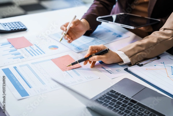 Obraz Two female business professionals in suits sit at desk, engaged in strategic discussion. They analyze financial planning, risk management, corporate growth while reviewing reports and market trends.