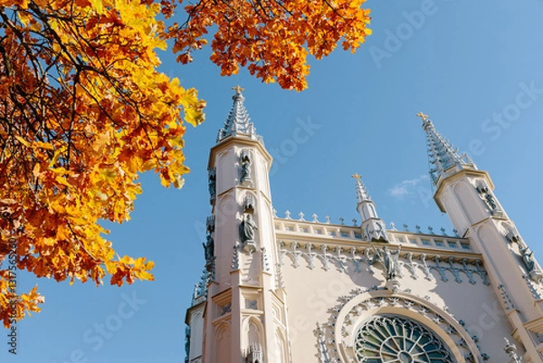 Fototapeta View of the spire of the church in the medieval Gothic style in the autumn park, the tops of the towers. Gothic chapel. Autumn