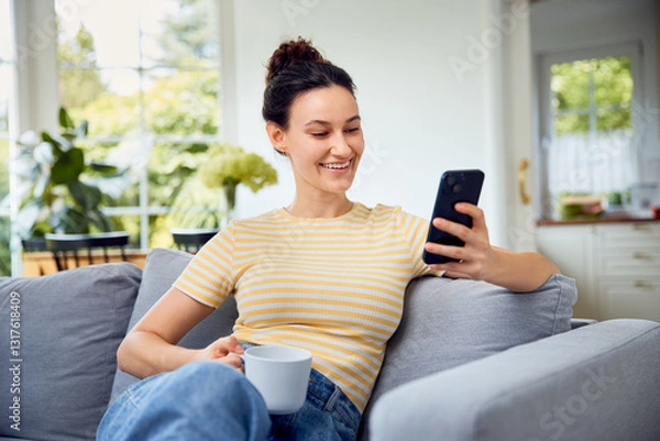 Fototapeta Happy woman using mobile phone  at home having coffe on sofa