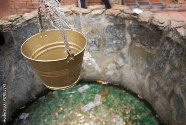 Obraz A golden bucket hanging above a little fountain made of stone.