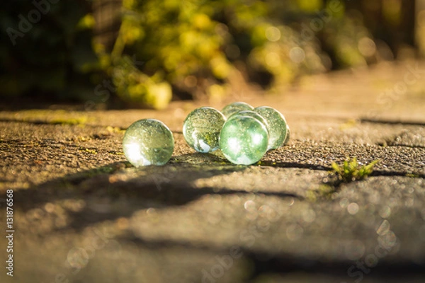 Obraz Translucent glass marbles on the sidewalk.
In the light of the setting sun.
Beautiful reflections in the marbles.