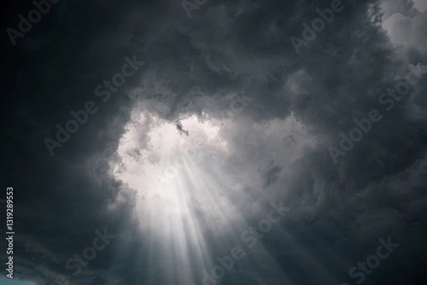 Fototapeta Rays of light through the hole in the dark stormy clouds in the sky.