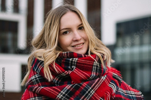 Fototapeta Happy woman with a scarf. Autumn. Autumn portrait of the beautiful girl. Office building. Fashionable portrait of a girl model with waving red scarf. Autumn portrait in the city.