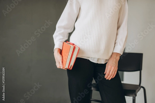 Obraz Woman Holding an Red Notebooks in a Cozy White Outfit