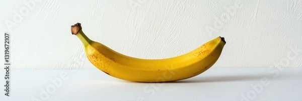 Obraz Minimalist display of a ripe banana on a soft white background with natural lighting highlighting its curves