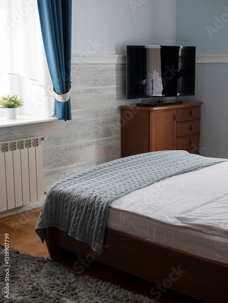 Fototapeta Serene bedroom featuring a neatly made bed, a wooden dresser, and a television. Concept of tranquility and comfort, importance of personal space and restful environments in daily life