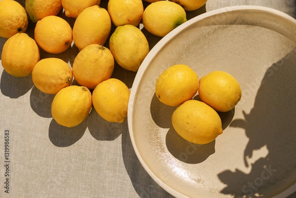 Fototapeta Multiple lemons spread across a surface with three placed in a plate,