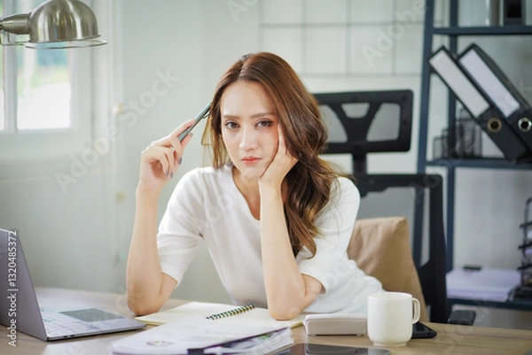 Obraz A woman is sitting at a desk with her head in her hands