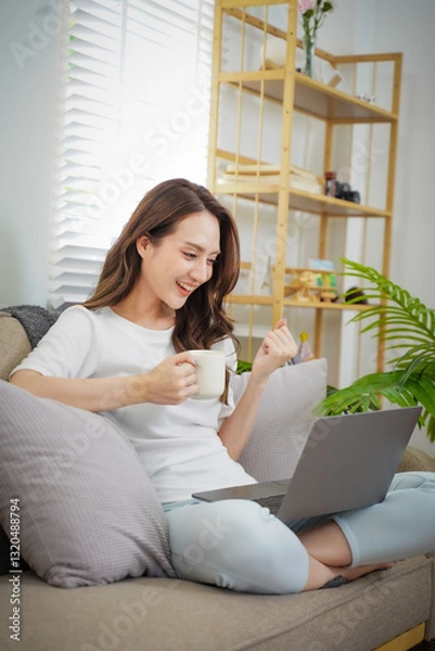 Obraz A woman is sitting on a couch with a laptop and a cup of coffee