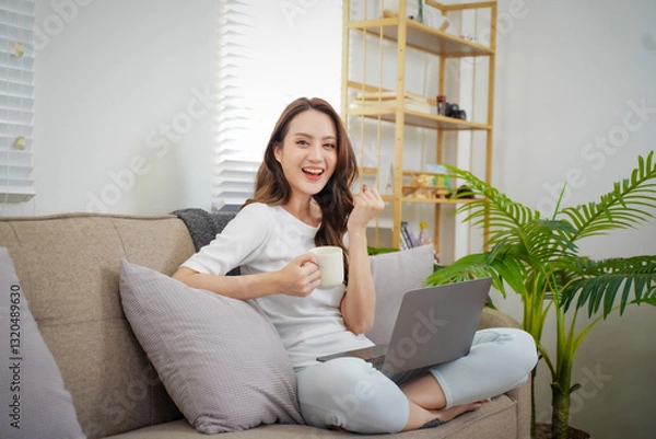 Fototapeta A woman is sitting on a couch with a laptop and a cup of coffee
