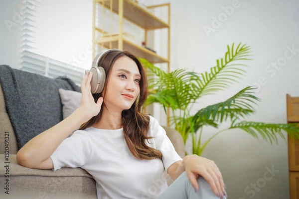 Obraz A woman is sitting on a couch with her headphones on