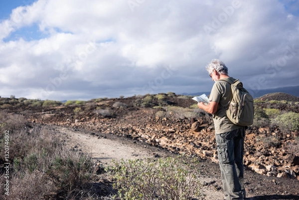 Fototapeta Senior white haired man enjoying outdoor adventure stops checking a map. Active mature man in mountain and countryside excursion