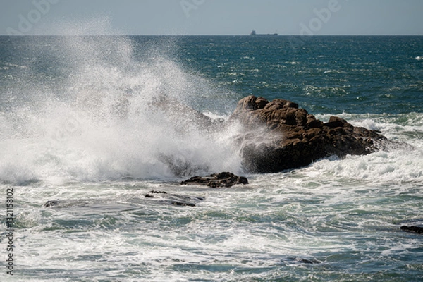 Obraz Powerful waves crash onto rocks along the coastline, creating a misty spray.