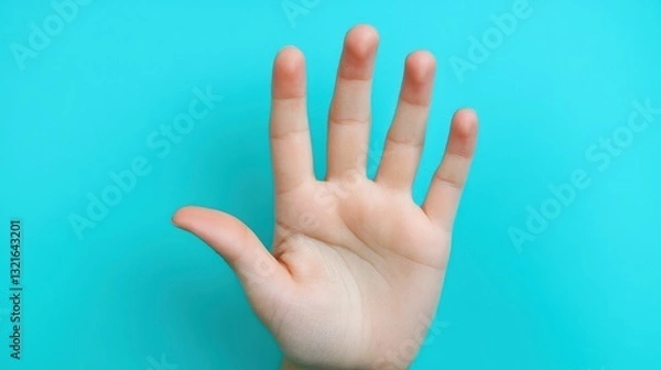 Fototapeta A raised hand shows five fingers extended, set against a vivid blue background. This gesture often signifies a request for attention or a signal to stop