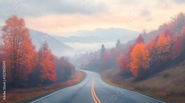 Fototapeta A winding road bordered by vibrant autumn trees, set against a misty landscape, evokes a serene fall atmosphere.