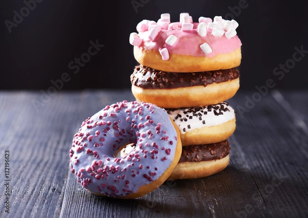 Fototapeta Close view at tasty donuts with blue, chocolate and vanilla icing on a dark wooden background. With copy space.