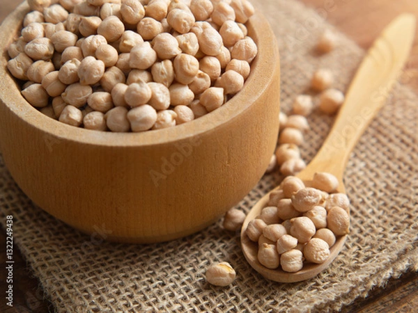 Fototapeta Close-up of a bowl filled with raw chickpeas surrounded by scattered legumes and a wooden spoon