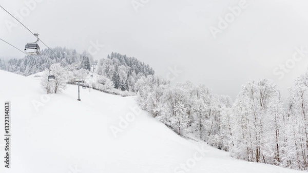 Fototapeta Winter landscape with snowy trees and a gondola railway to the top of the mountain, view during a mountain hike on a hiking trail. Winter day with cloudy and foggy weather.