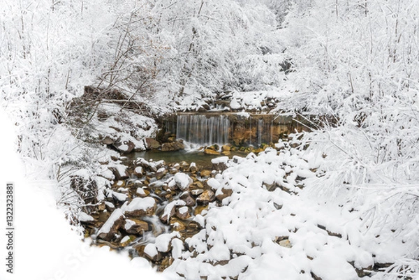Fototapeta Mountain river in winter, water flows down the riverbed over snow-covered rocks. Winter landscape on a mountain hiking trail.