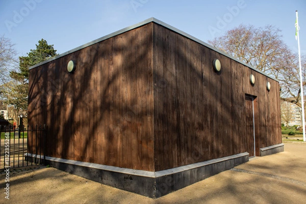 Fototapeta A wooden building located in the park, with trees behind it. It’s a sunny day.