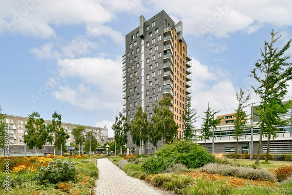 Obraz A sleek, modern residential building surrounded by vibrant greenery and well-kept paths, showcasing urban living blended with nature.