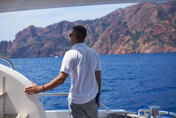 Fototapeta Deckhand enjoying scenic ocean view from yacht with rocky mountain backdrop