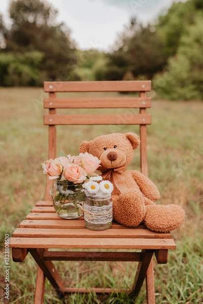 Fototapeta Teddy sitzt auf Holzstuhl mit Rosen und Gänseblümchen auf einer Wiese - Geburtstag, Freude, Liebe