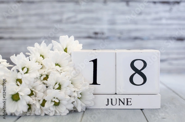 Fototapeta White wood calendar blocks with the date June 18th and white daisies. Selective focus with blurred background. 
