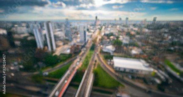 Fototapeta Blurred background of a large city with wide avenues, tall and low-density buildings seen through watermarked glass of a window